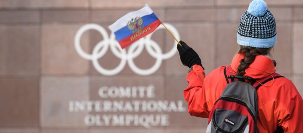 A supporter waves a Russian flag in front of the logo of the International Olympic Committee (IOC) at their headquarters on December 5, 2017 in Pully near Lausanne A supporter waves a Russian flag in front of the logo of the International Olympic Committee (IOC) at their headquarters on December 5, 2017 in Pully near Lausanne - Sputnik International