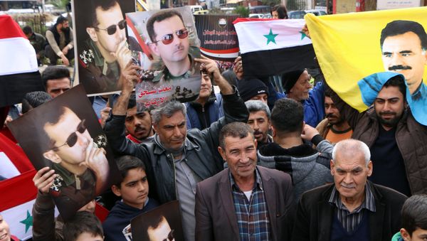 A picture taken on February 22, 2018 shows people waving the Syrian flag and portraits of President Bashar al-Assad and Kurdistan Worker's Party (PKK) leader Abdullah Ocalan as a convoy of pro-Syrian government fighters arrives in Syria's northern region of Afrin - Sputnik International