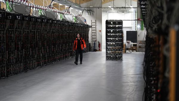 In this photo taken on Jan. 17, 2018, a worker walks along a row of computer rigs that run around the clock 'mining' bitcoin inside the Genesis Mining cryptocurrency mine in Keflavik, Iceland - Sputnik International