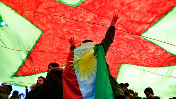 A demonstrator dressed in a Kurdistan flag cheers under a giant flag during a demonstration of Kurdish groups to protest against Turkey's offensive against Kurds in Syria's Afrin region, on March 3, 2018 in Berlin - Sputnik International