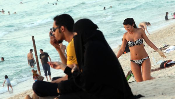 A foreign woman sunbathes near an Emirati couple on a beach in Dubai (File) - Sputnik International