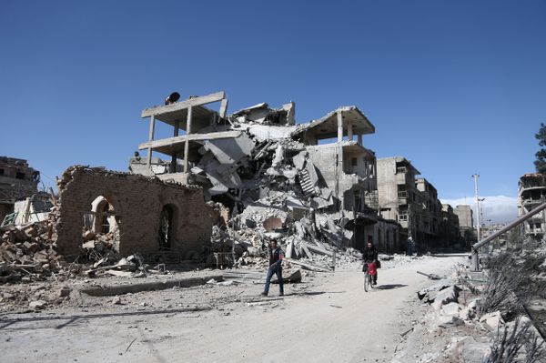 Syrians walk past destroyed buildings in the rebel-held town of Hamouria, in the besieged Eastern Ghouta region on the outskirts of the capital Damascus, on March 9, 2018 - Sputnik International