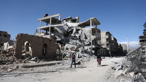 Syrians walk past destroyed buildings in the rebel-held town of Hamouria, in the besieged Eastern Ghouta region on the outskirts of the capital Damascus, on March 9, 2018 - Sputnik International