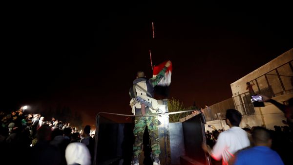 A member of forces of President Bashar al Assad holds a Syrian flag as buses carrying freed hostages and rebels who were evacuated from the rebel-held city of Douma drive at Wafideen camp in Damascus, Syria A member of forces of President Bashar al Assad holds a Syrian flag as buses carrying freed hostages and rebels who were evacuated from the rebel-held city of Douma drive at Wafideen camp in Damascus, Syria - Sputnik International