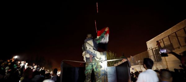 A member of forces of President Bashar al Assad holds a Syrian flag as buses carrying freed hostages and rebels who were evacuated from the rebel-held city of Douma drive at Wafideen camp in Damascus, Syria A member of forces of President Bashar al Assad holds a Syrian flag as buses carrying freed hostages and rebels who were evacuated from the rebel-held city of Douma drive at Wafideen camp in Damascus, Syria - Sputnik International