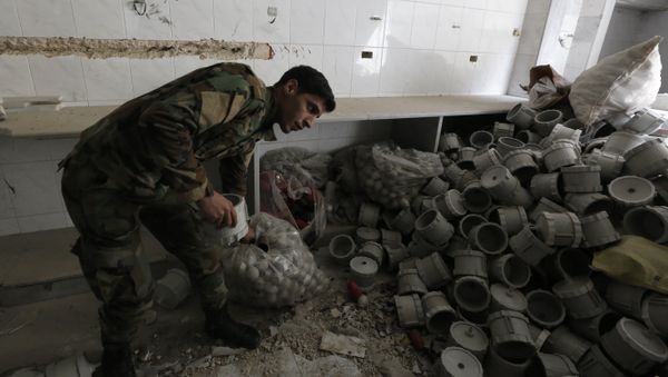 A member of the Syrian government forces looks at materials they say were used by opposition fighters to make weapons in the former rebel-held town of Zamalka in Eastern Ghouta, on the outskirts of the capital Damascus on April 11, 2018 - Sputnik International