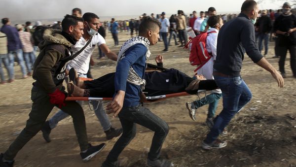 Palestinian protesters evacuate a wounded woman during clashes with Israeli troops along Gaza's border with Israel, Friday, April 13, 2018. - Sputnik International