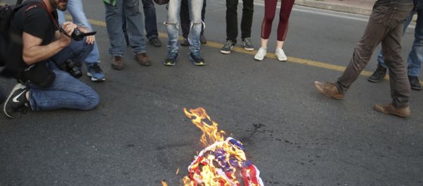Protesters burn an American flag outside the U.S. Embassy in Athens, Friday, April 13, 2018, during a rally against possible western military intervention in Syria Protesters burn an American flag outside the U.S. Embassy in Athens, Friday, April 13, 2018, during a rally against possible western military intervention in Syria - Sputnik International