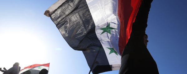 A Syrian government supporter holds up a Syrian national flag as he chants slogans against U.S. President Trump during demonstrations following a wave of U.S., British and French military strikes to punish President Bashar Assad for suspected chemical attack against civilians, in Damascus, Syria, Saturday, April 14, 2018 - Sputnik International