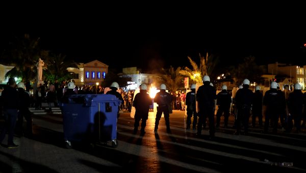 A garbage bin burns as riot police officers stand guard separating protesting groups of locals and refugees demonstrating against conditions in Moria camp and delays in asylum applications, in the city of Mytilene on the island of Lesbos, Greece, April 22, 2018 A garbage bin burns as riot police officers stand guard separating protesting groups of locals and refugees demonstrating against conditions in Moria camp and delays in asylum applications, in the city of Mytilene on the island of Lesbos, Greece, April 22, 2018 - Sputnik International