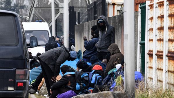 Migrants gather by the ringroad leading to the harbour on March 30, 2018 in Calais, near a police van patrolling (Rear L) - Sputnik International