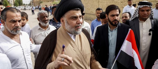 Iraqi Shiite cleric and leader Moqtada al-Sadr (C-L) shows his ink-stained index finger and holds a national flag while surrounded by people outside a polling station in the central holy city of Najaf on May 12, 2018 as the country votes in the first parliamentary election since declaring victory over the Islamic State (IS) group - Sputnik International