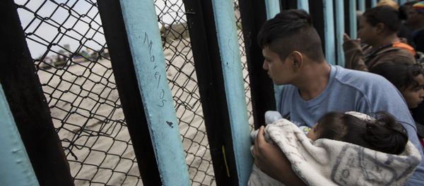 In this April 29, 2018 file photo, a member of the Central American migrant caravan, holding a child, looks through the border wall toward a group of people gathered on the U.S. side, as he stands on the beach where the border wall ends in the ocean, in Tijuana, Mexico, Sunday, April 29, 2018 In this April 29, 2018 file photo, a member of the Central American migrant caravan, holding a child, looks through the border wall toward a group of people gathered on the U.S. side, as he stands on the beach where the border wall ends in the ocean, in Tijuana, Mexico, Sunday, April 29, 2018 - Sputnik International