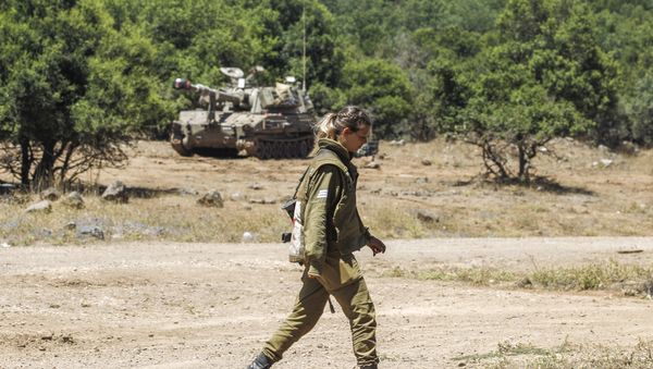 An Israeli soldier walks as a mobile artillery piece is seen deployed in the background near the border with Syria in the Israeli-annexed Syrian Golan Heights on July 1, 2018 An Israeli soldier walks as a mobile artillery piece is seen deployed in the background near the border with Syria in the Israeli-annexed Syrian Golan Heights on July 1, 2018 - Sputnik International
