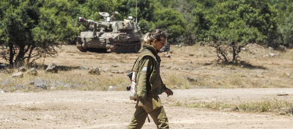 An Israeli soldier walks as a mobile artillery piece is seen deployed in the background near the border with Syria in the Israeli-annexed Syrian Golan Heights on July 1, 2018 - Sputnik International