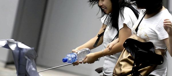 In this photo released by China's Xinhua News Agency, passers-by struggle in the street with an umbrella almost blown off in Hong Kong, south China (File) - Sputnik International