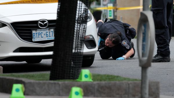 A police officer looks for evidence under a car while investigating a mass shooting on Danforth Avenue in Toronto, Canada, July 23, 2018. A police officer looks for evidence under a car while investigating a mass shooting on Danforth Avenue in Toronto, Canada, July 23, 2018. - Sputnik International