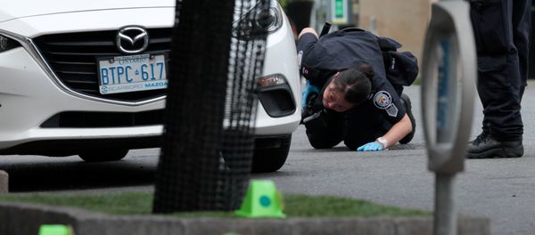 A police officer looks for evidence under a car while investigating a mass shooting on Danforth Avenue in Toronto, Canada, July 23, 2018. - Sputnik International