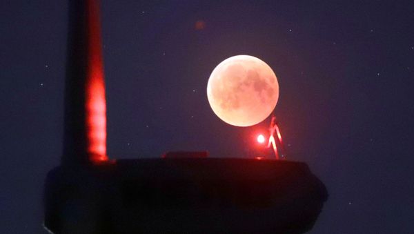 The blades from a wind turbine are silhouetted against the moon in the sky in Novogrudok, Belarus, during a total lunar eclipse on Saturday, July 28, 2018. Skywatchers around much of the world are looking forward to a complete lunar eclipse that will be the longest this century.  - Sputnik International
