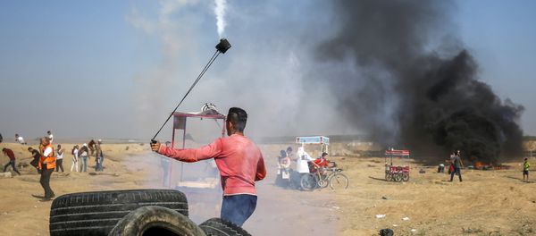 A Palestinian protester uses a slingshot to throw back a tear gas canister towards Israeli forces during clashes following a demonstration along the border east of Gaza City on July 6, 2018 A Palestinian protester uses a slingshot to throw back a tear gas canister towards Israeli forces during clashes following a demonstration along the border east of Gaza City on July 6, 2018 - Sputnik International