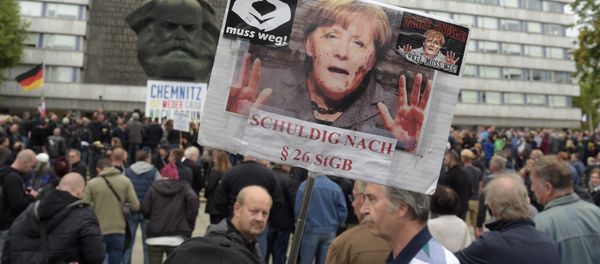 A protestor holds a poster with a photo of Angela Merkel reading 'Merkel must go and referring she is guilty of incitement in Chemnitz, eastern Germany, Saturday, Sept. 1, 2018, after several nationalist groups called for marches protesting the killing of a German man last week, allegedly by migrants from Syria and Iraq A protestor holds a poster with a photo of Angela Merkel reading 'Merkel must go and referring she is guilty of incitement in Chemnitz, eastern Germany, Saturday, Sept. 1, 2018, after several nationalist groups called for marches protesting the killing of a German man last week, allegedly by migrants from Syria and Iraq - Sputnik International