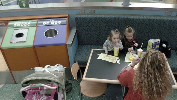 Lena Miller, right, with her daughters Kennedi, 2, left, and Kelsea Miller, 6, eat their lunch next to a new specially labeled bin containing a biodegradable bag at an eating area on the departure concourse at Portland International Airport in Portland, Ore., Thursday Nov.20, 2008. The airport is ramping up a three-year-old program to install food-only trash cans. The food waste is collected in biodegradable bags and given to the city to use as compost, said Stan Jones, aviation environmental compliance manager at the airport. - Sputnik International