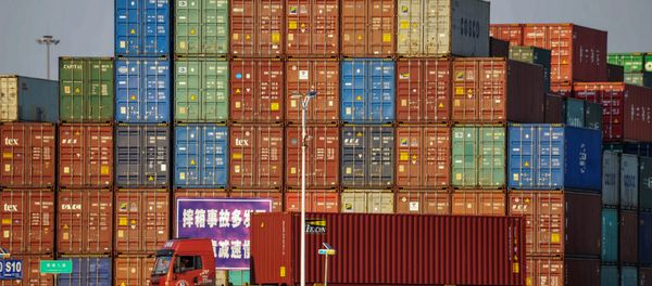 A truck transports a container next to stacked containers at a port in Qingdao in China's eastern Shandong province on October 12, 2018 - Sputnik International