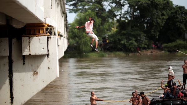 A Honduran migrant jumps from the bridge that connects Mexico and Guatemala to avoid the border checkpoint in Ciudad Hidalgo - Sputnik International