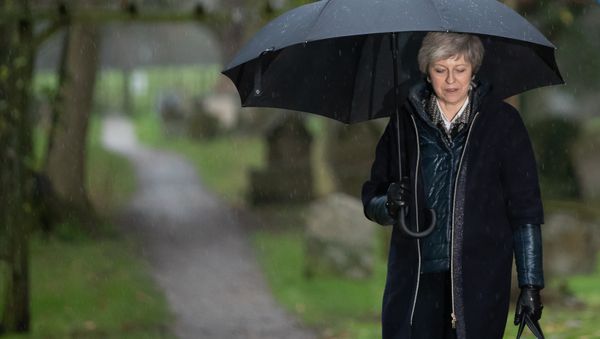 Britain's Prime Minister Theresa May shelters from the rain under an umbrella after attending a church service near to her Maidenhead constituency, west of London on December 9, 2018 Britain's Prime Minister Theresa May shelters from the rain under an umbrella after attending a church service near to her Maidenhead constituency, west of London on December 9, 2018 - Sputnik International