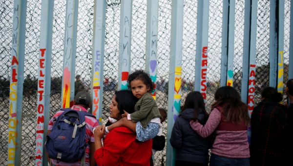 A woman carries her son as she looks at people taking part in a gathering in support of the migrant caravan in San Diego, U.S., close to the border wall between the United States and Mexico, in Tijuana, Mexico December 10, 2018 - Sputnik International