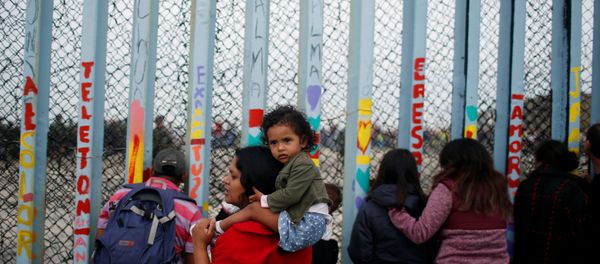 A woman carries her son as she looks at people taking part in a gathering in support of the migrant caravan in San Diego, U.S., close to the border wall between the United States and Mexico, in Tijuana, Mexico December 10, 2018 A woman carries her son as she looks at people taking part in a gathering in support of the migrant caravan in San Diego, U.S., close to the border wall between the United States and Mexico, in Tijuana, Mexico December 10, 2018 - Sputnik International