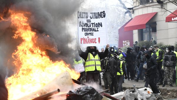 A protestor wearing a yellow vest holds a banner during the yellow vests rally in Paris, France. So-called yellow vest protests — named after the obligatory attribute of French cars — started in mid-November and have evolved into a large-scale movement against government policies and rising living costs. - Sputnik International