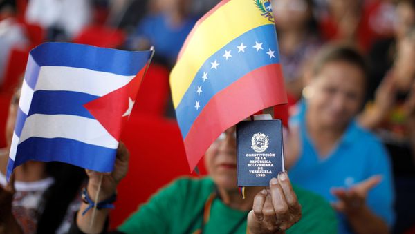 A supporter of Venezuela's President Nicolas Maduro holding a copy of the Venezuelan constitution and flags of Venezuela and Cuba, takes part in a gathering in support of his government outside the Miraflores Palace in Caracas, Venezuela January 26, 2019 A supporter of Venezuela's President Nicolas Maduro holding a copy of the Venezuelan constitution and flags of Venezuela and Cuba, takes part in a gathering in support of his government outside the Miraflores Palace in Caracas, Venezuela January 26, 2019 - Sputnik International