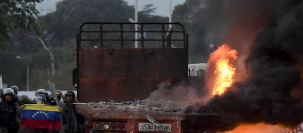 Venezuelan security forces display a national flag next to a truck which was burnt during the weekend when trying to enter the country with humanitarian aid, during clashes with supporters of Venezuelan opposition leader Juan Guaido on the Venezuelan side of the Francisco de Paula Santander International Bridge, as seen from Cucuta, Colombia, on February 25, 2019. Venezuelan security forces display a national flag next to a truck which was burnt during the weekend when trying to enter the country with humanitarian aid, during clashes with supporters of Venezuelan opposition leader Juan Guaido on the Venezuelan side of the Francisco de Paula Santander International Bridge, as seen from Cucuta, Colombia, on February 25, 2019. - Sputnik International