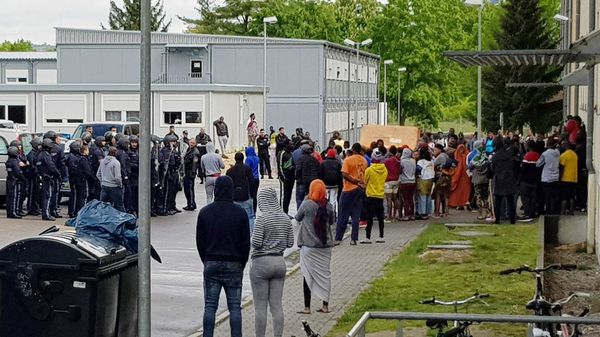 German police officers and migrants stand in front of an asylum center after a woman was found dead in the center in Regensburg, Germany, Saturday, May 11, 2019 - Sputnik International