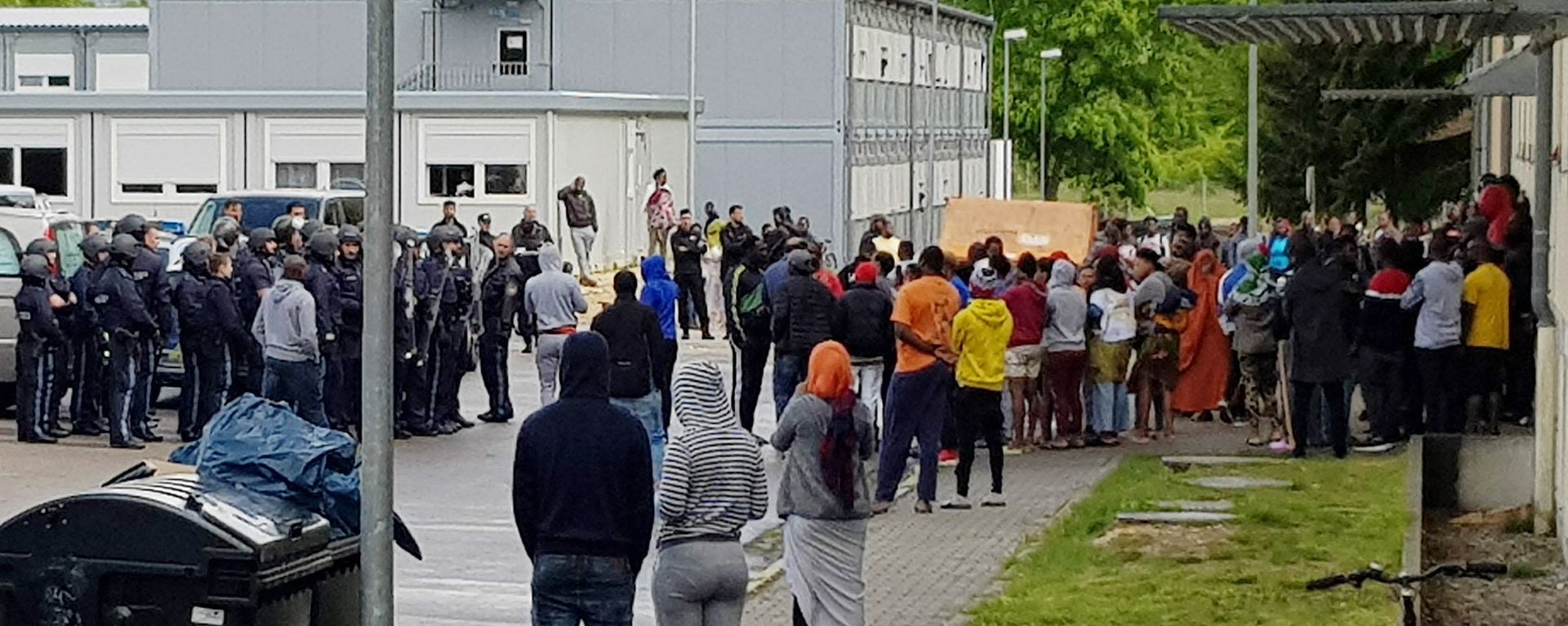 German police officers and migrants stand in front of an asylum center after a woman was found dead in the center in Regensburg, Germany, Saturday, May 11, 2019 German police officers and migrants stand in front of an asylum center after a woman was found dead in the center in Regensburg, Germany, Saturday, May 11, 2019 - Sputnik International, 1920, 26.11.2021