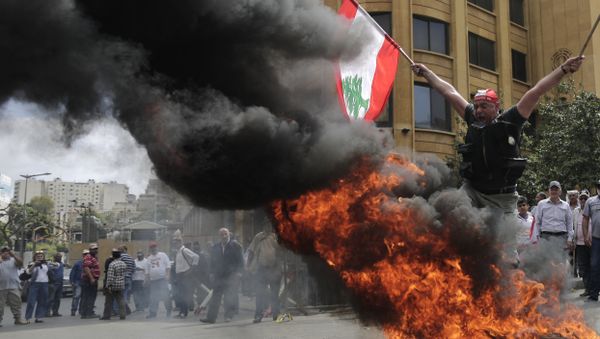 A Lebanese retired soldier holds a Lebanese national flag as he jump over burning tires during a protest in front of the government building during a cabinet meeting to discuss an austerity budget, in Beirut, Lebanon - Sputnik International