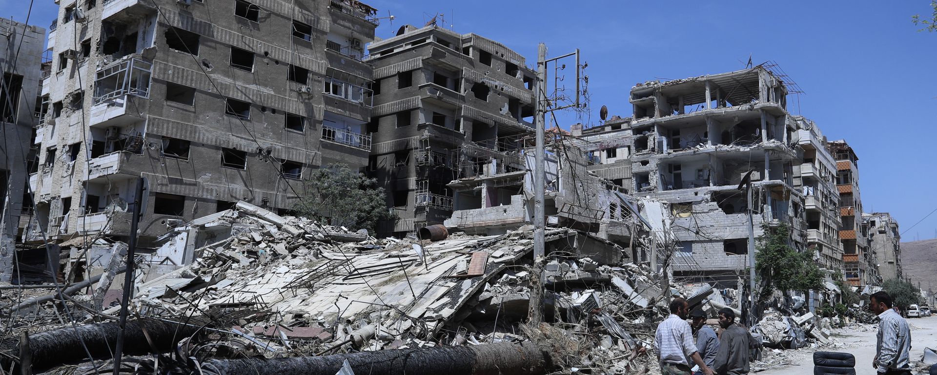 Syrians stand in front of damaged buildings in the Damascus suburb of Douma, the site of an alleged chemical weapons attack, 16 April 2018 - Sputnik International, 1920, 21.01.2020