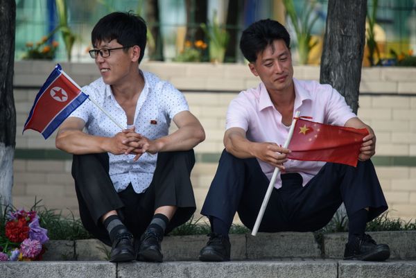 Two Men Sit Holding North Korean and Chinese Flags Near Kim Il Sung Square in Pyongyang Two Men Sit Holding North Korean and Chinese Flags Near Kim Il Sung Square in Pyongyang - Sputnik International