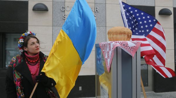 A woman holds a Ukraine flag and looks up at the traditional Ukrainian bread and salt in front of the US embassy in Kiev, Ukraine, Friday, Jan. 20, 2017, in support of Donald Trump hours before he is to be sworn in as president of the United States. - Sputnik International
