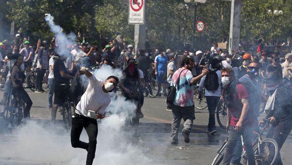   A protester returns a tear gas canister to police during clashes in Santiago, Chile on 20 October 2019. - Sputnik International