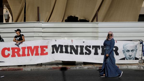 A woman walks past a banner depicting Israeli Prime Minister Benjamin Netanyahu and the words Crime Minister outside the Justice Ministry A woman walks past a banner depicting Israeli Prime Minister Benjamin Netanyahu and the words Crime Minister outside the Justice Ministry - Sputnik International
