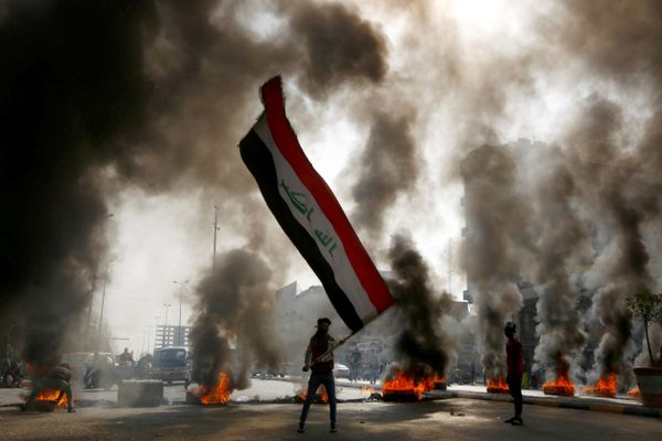 A protester holds an Iraqi flag amid a cloud of smoke from burning tyres during ongoing anti-government protests in Najaf, Iraq on 26 November 2019. A protester holds an Iraqi flag amid a cloud of smoke from burning tyres during ongoing anti-government protests in Najaf, Iraq on 26 November 2019. - Sputnik International