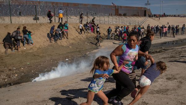 Maria Meza, a 40-year-old migrant woman from Honduras, part of a caravan of thousands from Central America trying to reach the United States, runs away from tear gas with her five-year-old twin daughters Saira Mejia Meza (L) and Cheili Mejia Meza (R) in front of the border wall between the U.S and Mexico, in Tijuana, Mexico, November 25, 2018 - Sputnik International