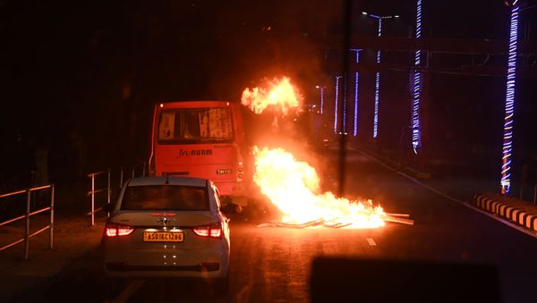 In this photo taken on 12 December 2019, a bus and car drive past a burning barricade set up by demonstrators following protests against the Citizenship Amendment Bill (CAB) in Guwahati. - Sputnik International