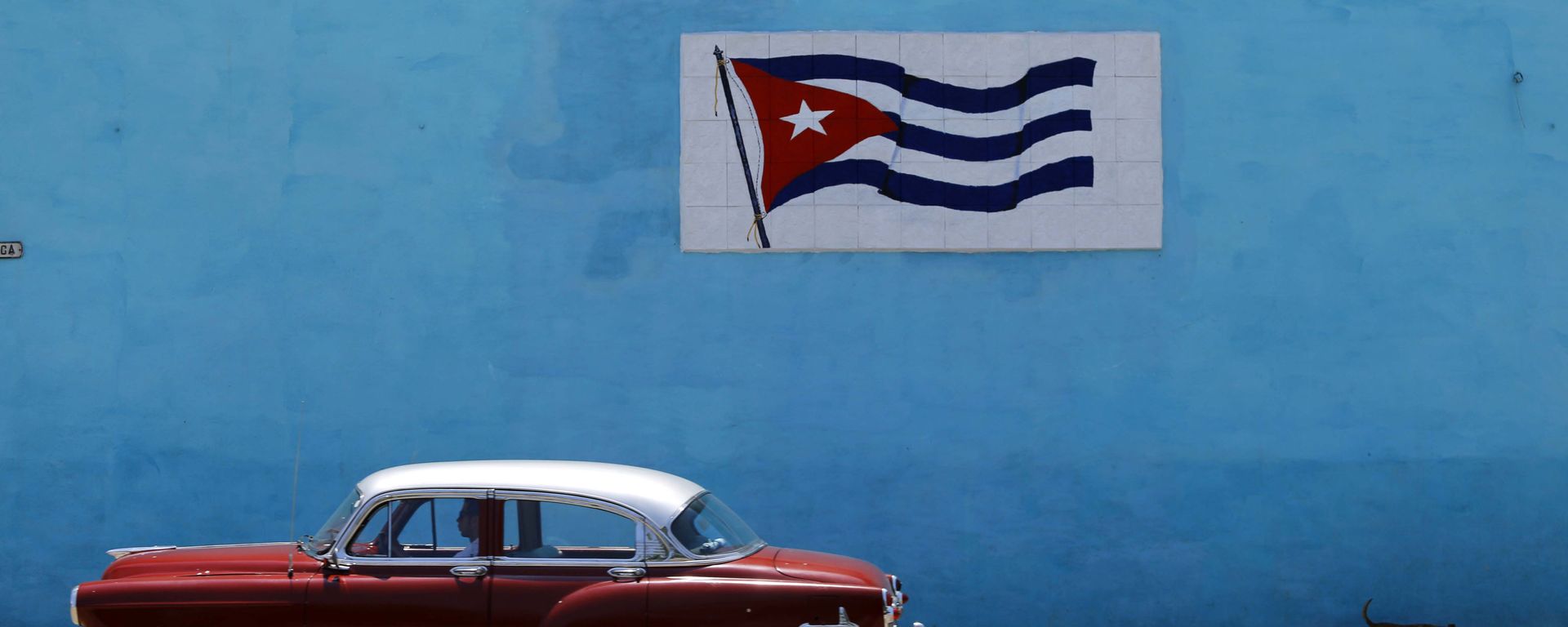 A driver steers his classic car past a wall decorated with a Cuban flag in Havana A driver steers his classic car past a wall decorated with a Cuban flag in Havana - Sputnik International, 1920, 13.03.2021