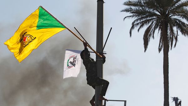 A member of the Hashd al-Shaabi paramilitary forces holds a flag of the Kataib Hezbollah militia group during a protest to condemn air strikes on their bases, in Baghdad, Iraq, 31 December 2019. A member of the Hashd al-Shaabi paramilitary forces holds a flag of the Kataib Hezbollah militia group during a protest to condemn air strikes on their bases, in Baghdad, Iraq, 31 December 2019. - Sputnik International
