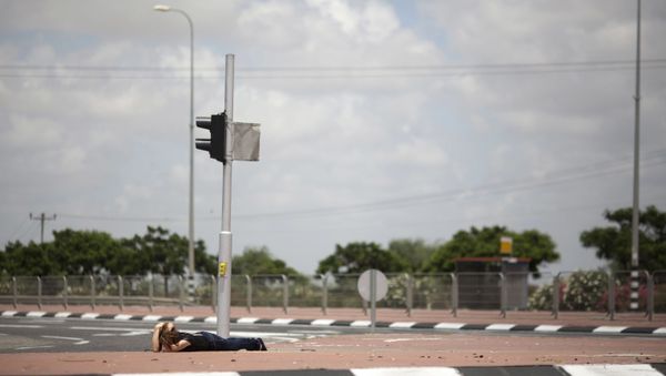 An Israeli woman takes cover as siren alarming sounds warning of rocket attacks by Palestinians militants from Gaza Strip in Ashkelon, southern Israel, Monday, July 14, 2014. - Sputnik International
