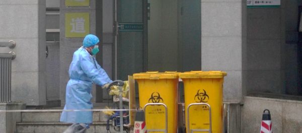 FILE - In this Wednesday, Jan. 22, 2020, file photo, a staff member moves bio-waste containers past the entrance of the Wuhan Medical Treatment Center in Wuhan, China, where some people infected with a new virus are being treated.  - Sputnik International