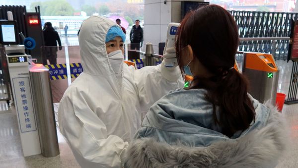 A worker in protective suits checks the temperature of a passenger arriving at the Xianning North Station on the eve of the Chinese Lunar New Year celebrations, in Xianning, a city bordering Wuhan to the north, in Hubei province, China January 24, 2020. - Sputnik International